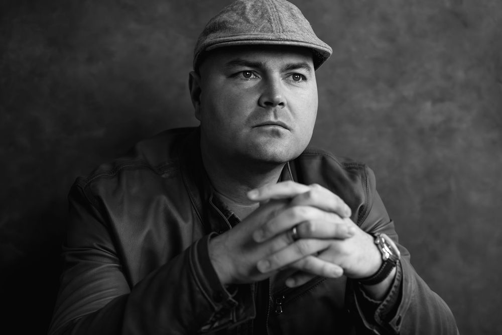 A black and white collage of portraits shows a person in casual attire against a dark background.