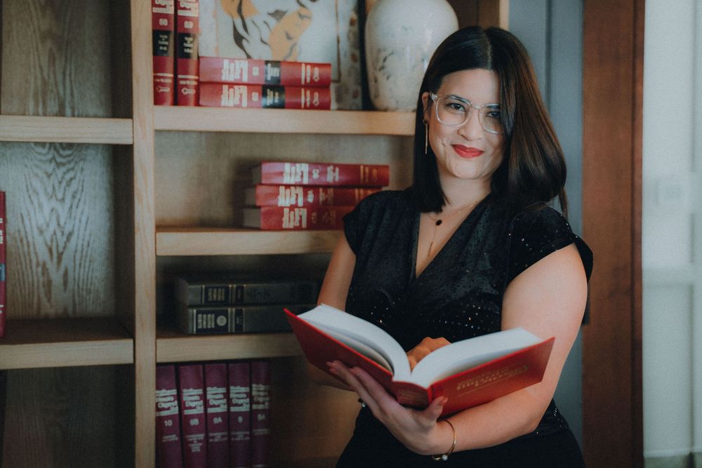 Captivating series of library portraits showing a reader in a black dress posed among red books on wooden shelves.