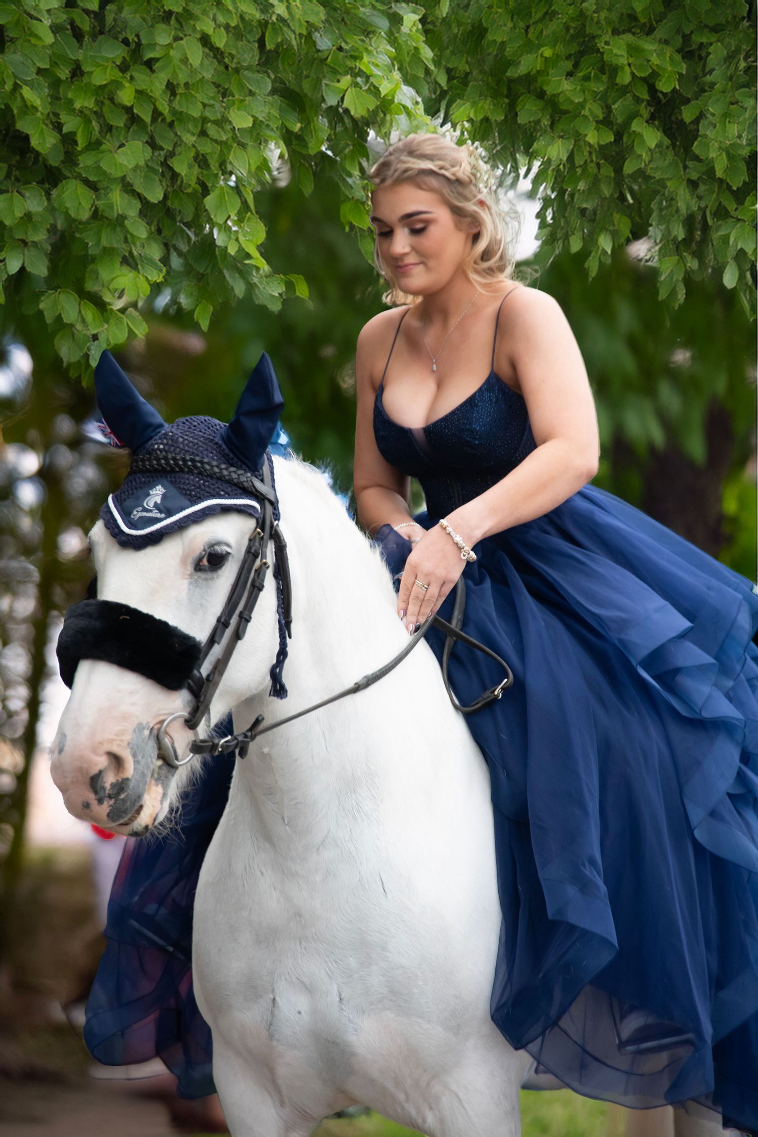 A collage of four photos showing someone in a navy blue dress sitting on a white horse during an outdoor photoshoot.