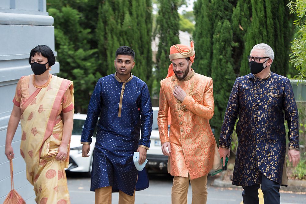 Wedding party members wearing traditional Indian and South Asian formal attire walking outdoors in a garden setting.