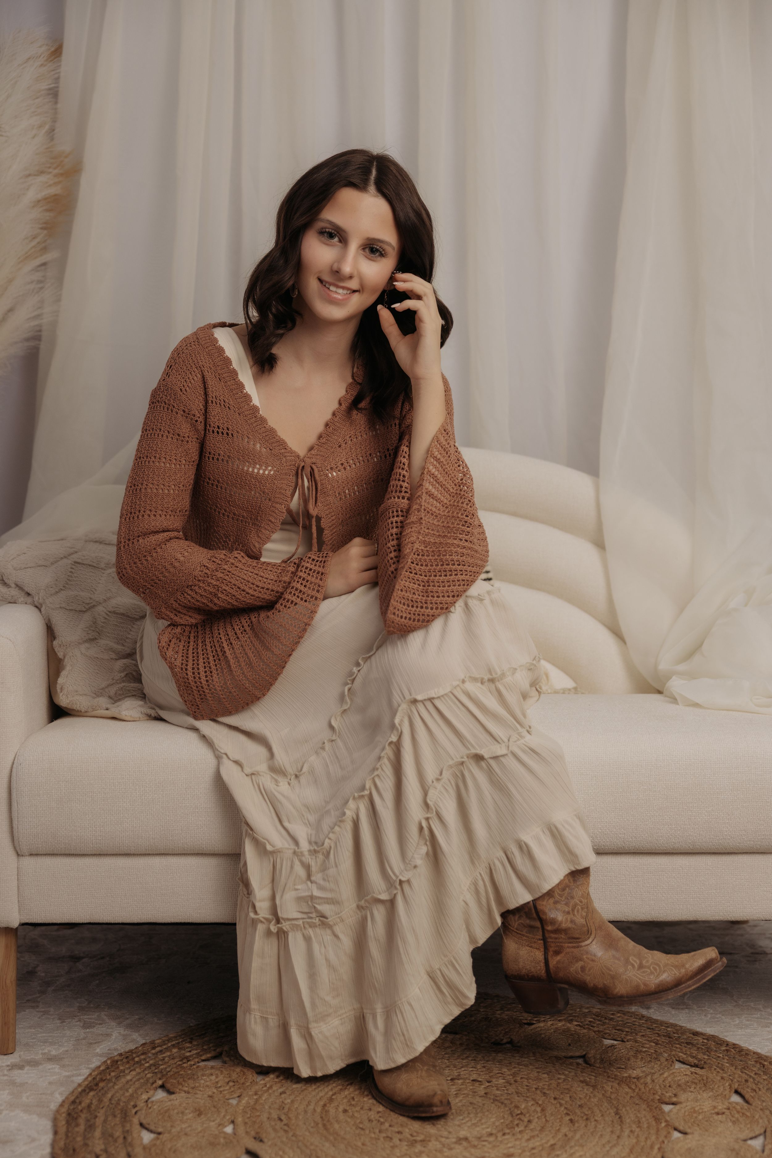 Cozy indoor portraits with brown sweater and cream ruffle dress on textured round rug.