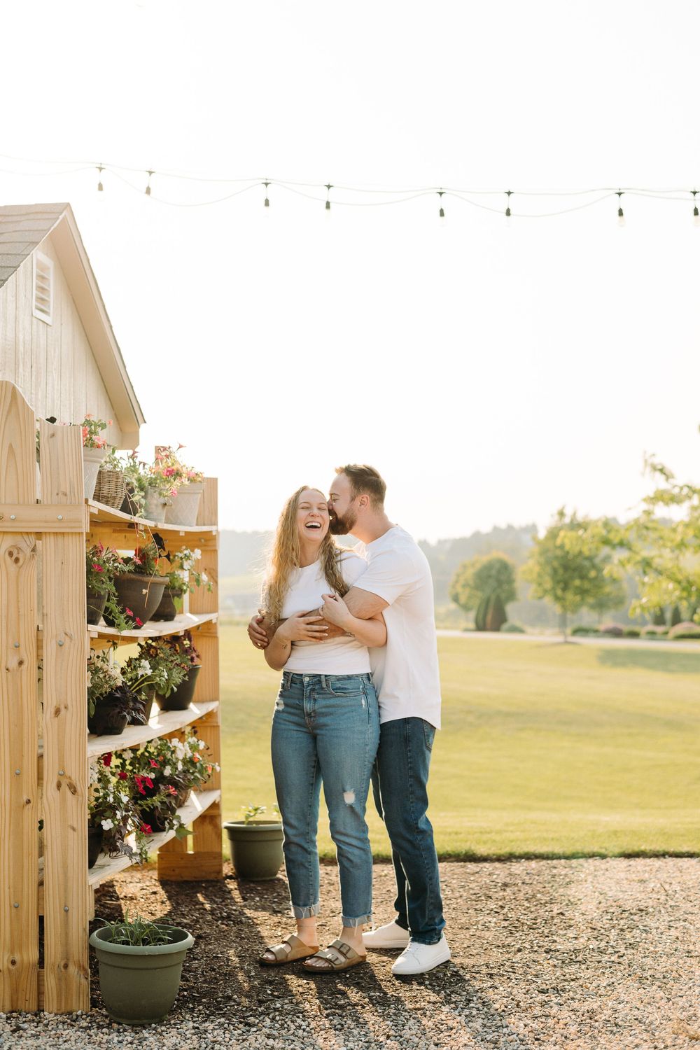 Couple embraces near rustic wooden planter boxes filled with colorful flowers in golden sunset light.