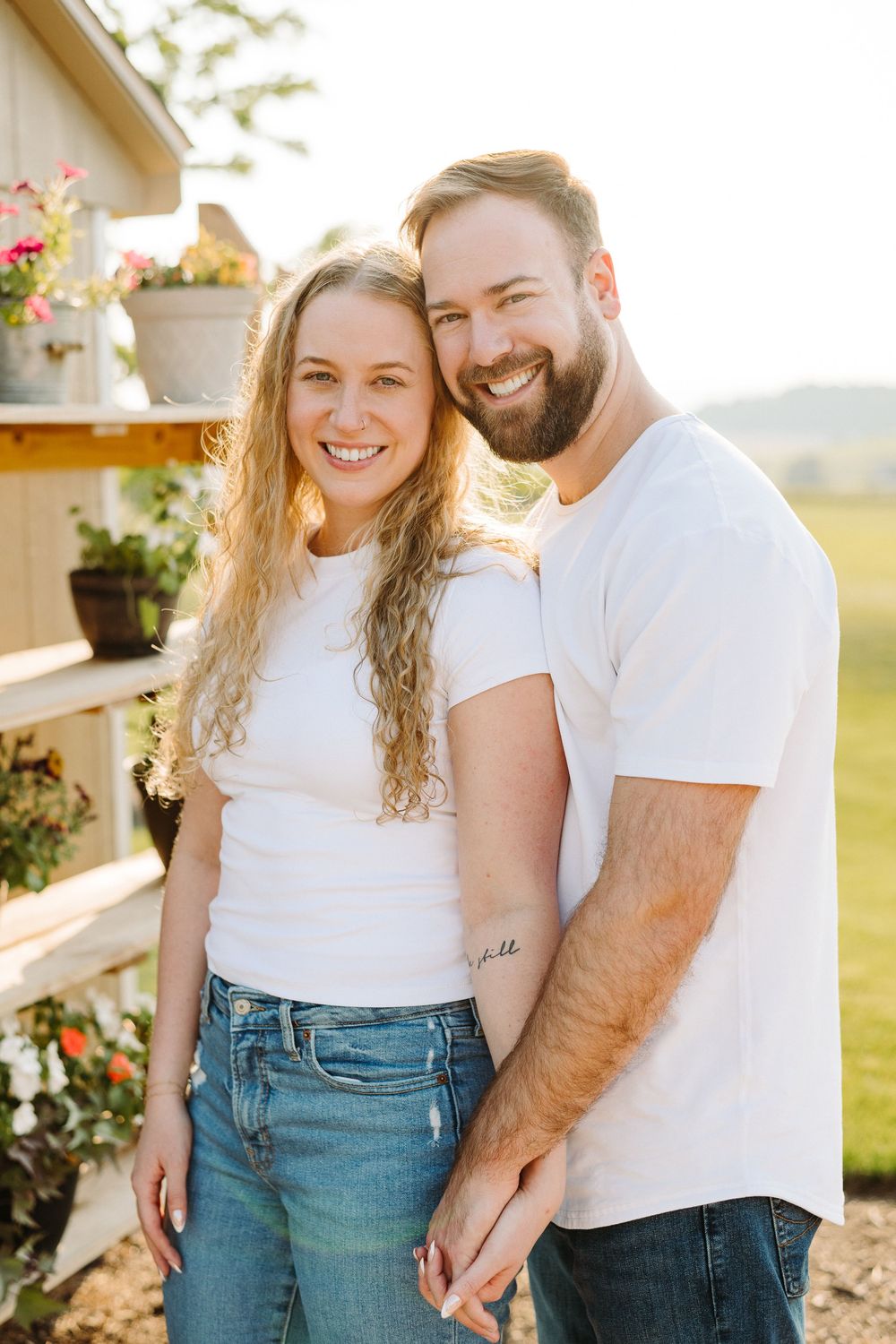 Couple in matching white shirts and jeans embracing and laughing together in a sunlit garden setting.