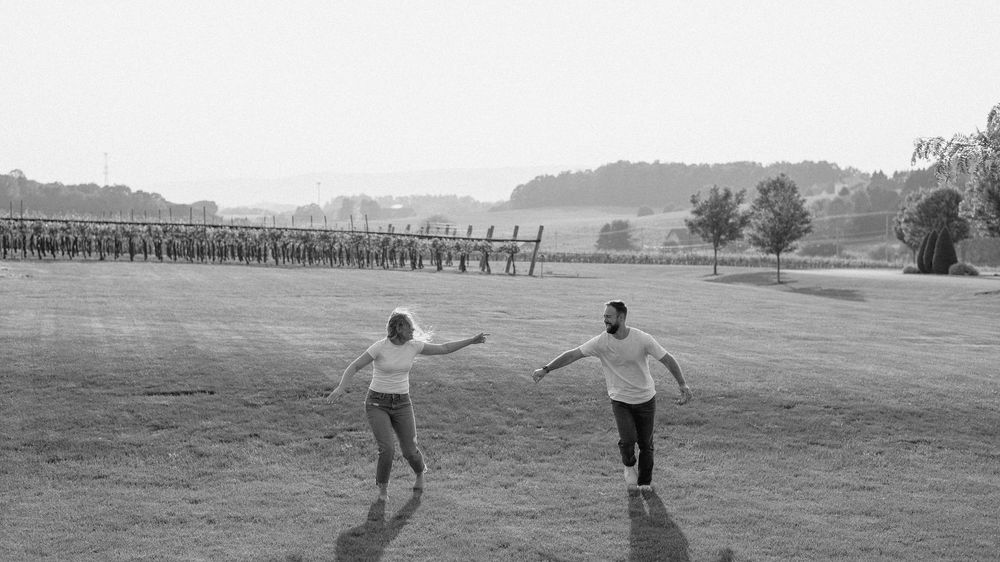 Silhouettes of people walking across a scenic rural landscape with wooden fences at dusk.