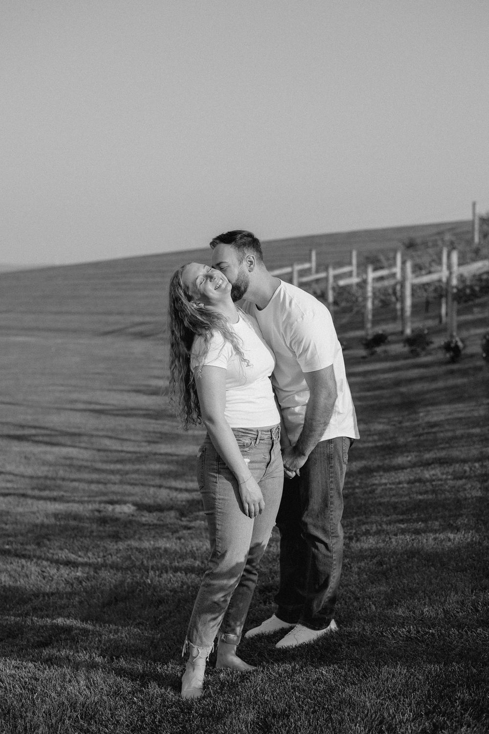 Black and white photo series of couple laughing and embracing on a grassy hillside.