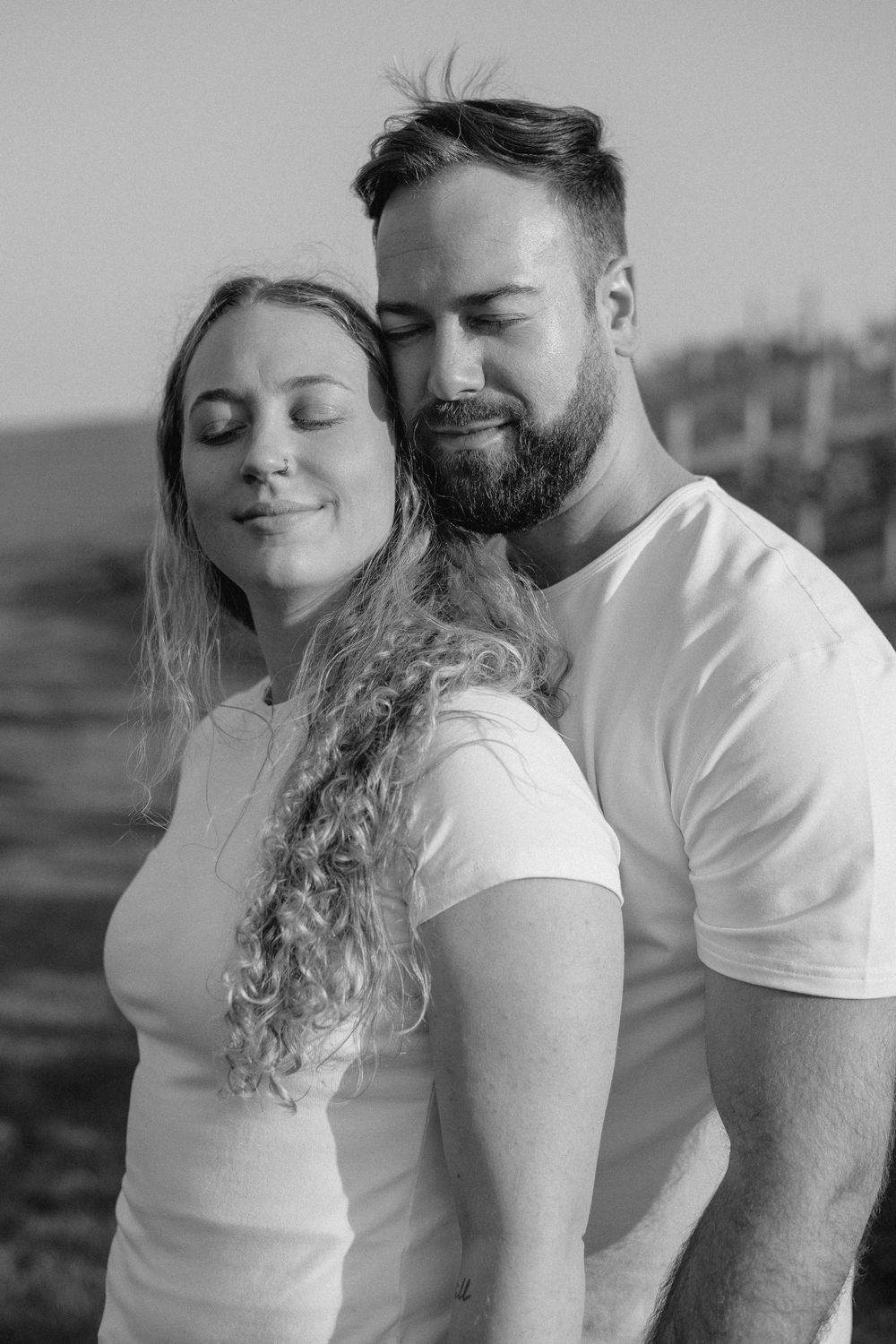 A romantic black and white portrait of a couple in white shirts embracing outdoors.