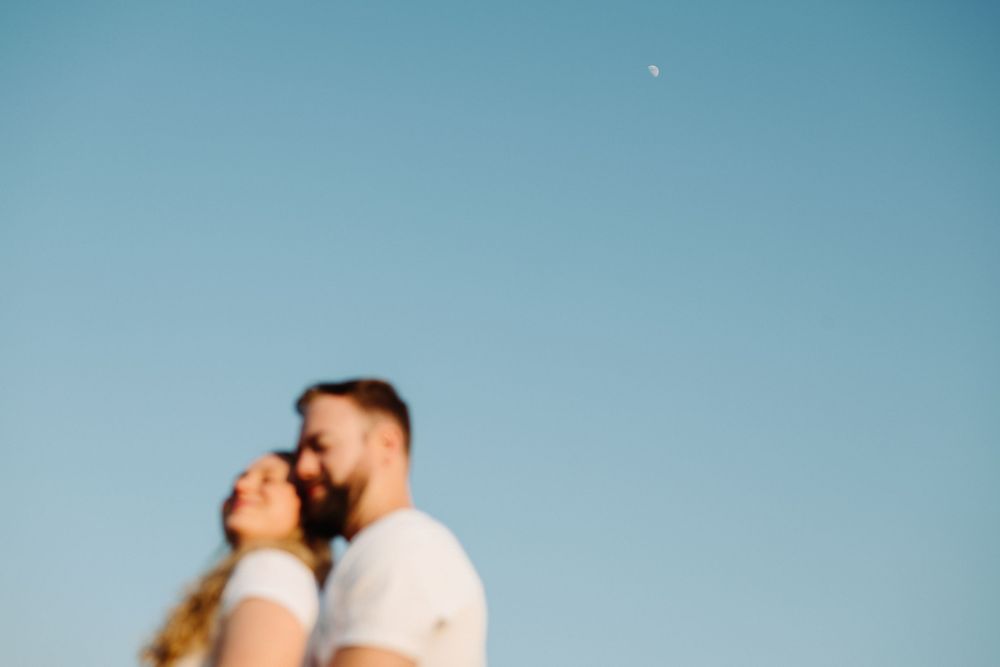 A blurred romantic couple embraces against a bright blue summer sky.