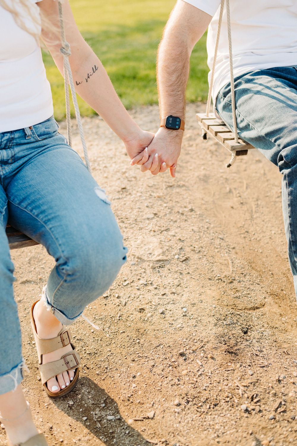 Close up of hands reaching towards each other on a swing set, with one person wearing a smartwatch and denim.