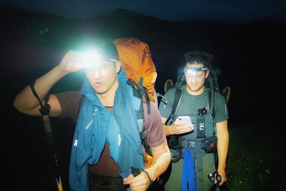Nighttime hikers using headlamps on dark mountain trail.