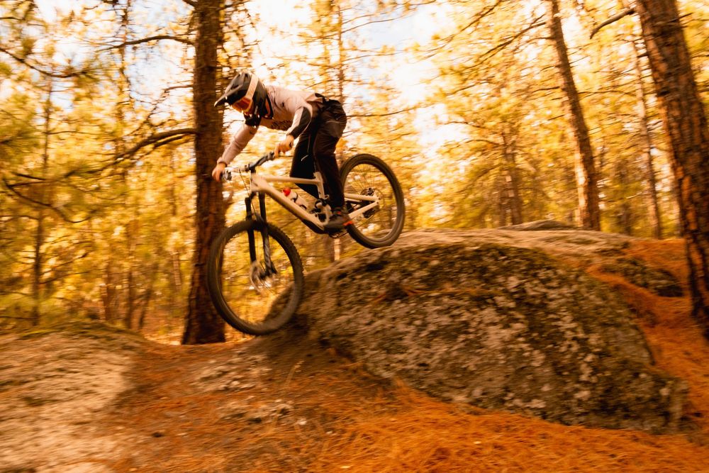 Mountain biker performing aerial stunts at sunset in wooded trail.