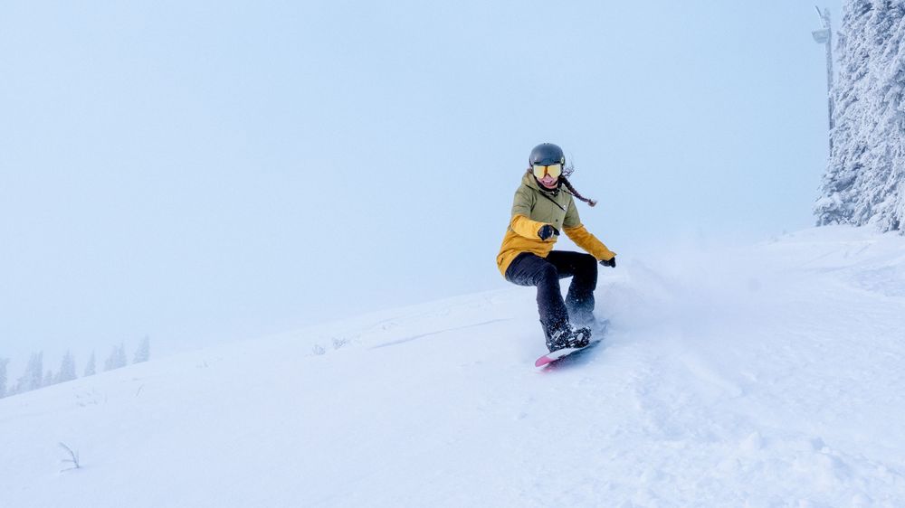 Snowboarder in yellow jacket carving down a snowy ski slope on a clear winter day.