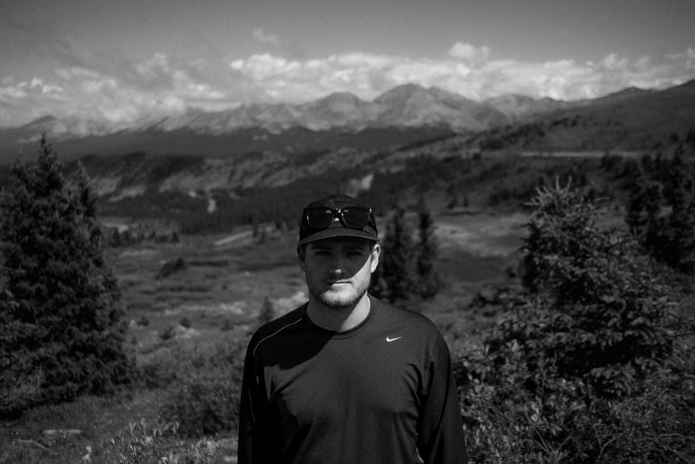 Black and white portrait of a person in a hat with mountain landscape behind.