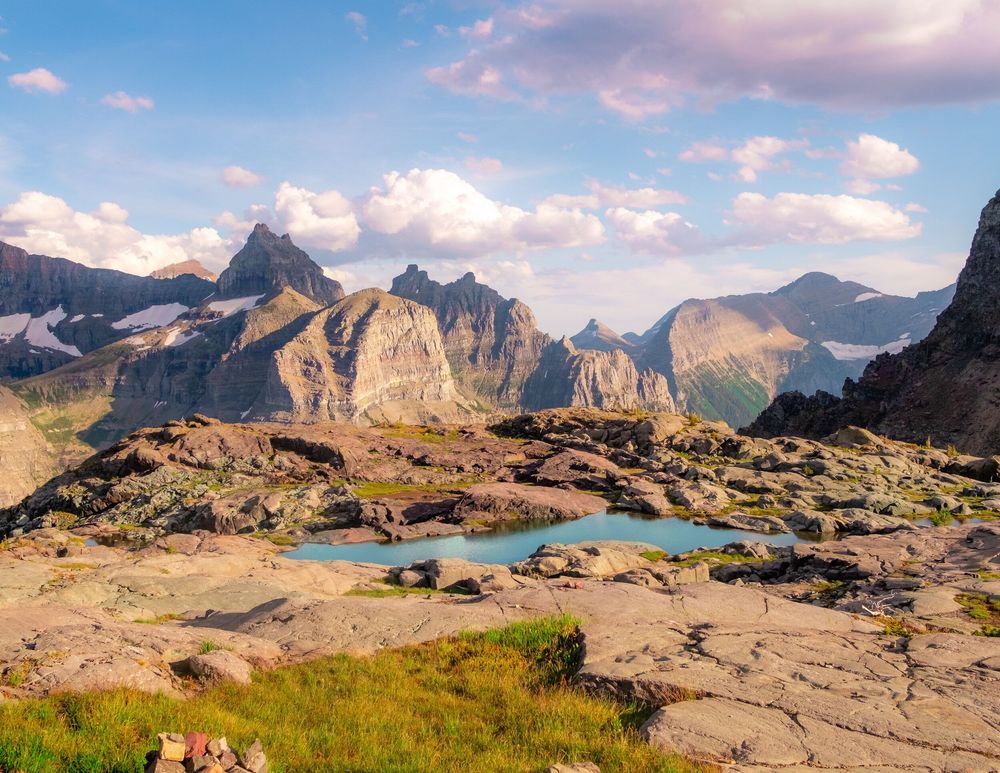 Rocky mountain vista with dramatic peaks and meadows under partly cloudy skies.