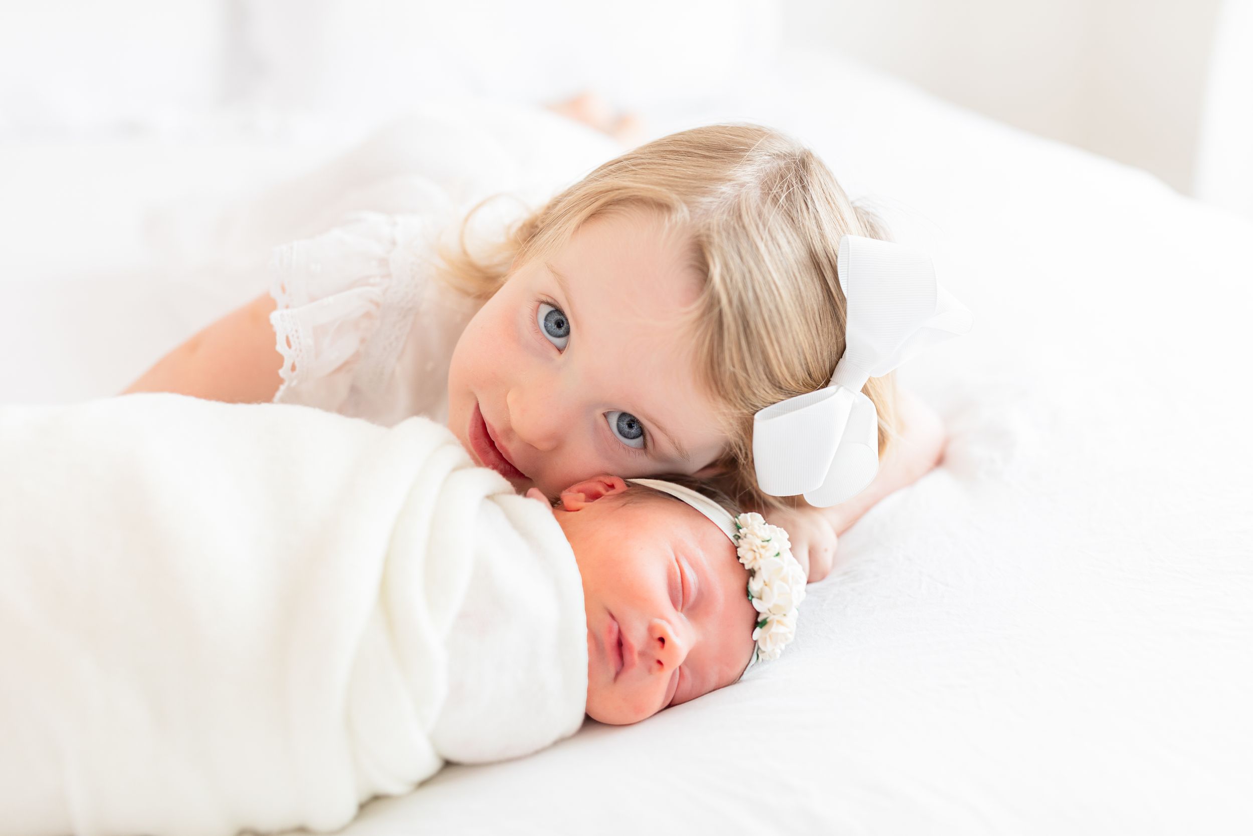 Baby lying on white blanket with soft natural lighting.