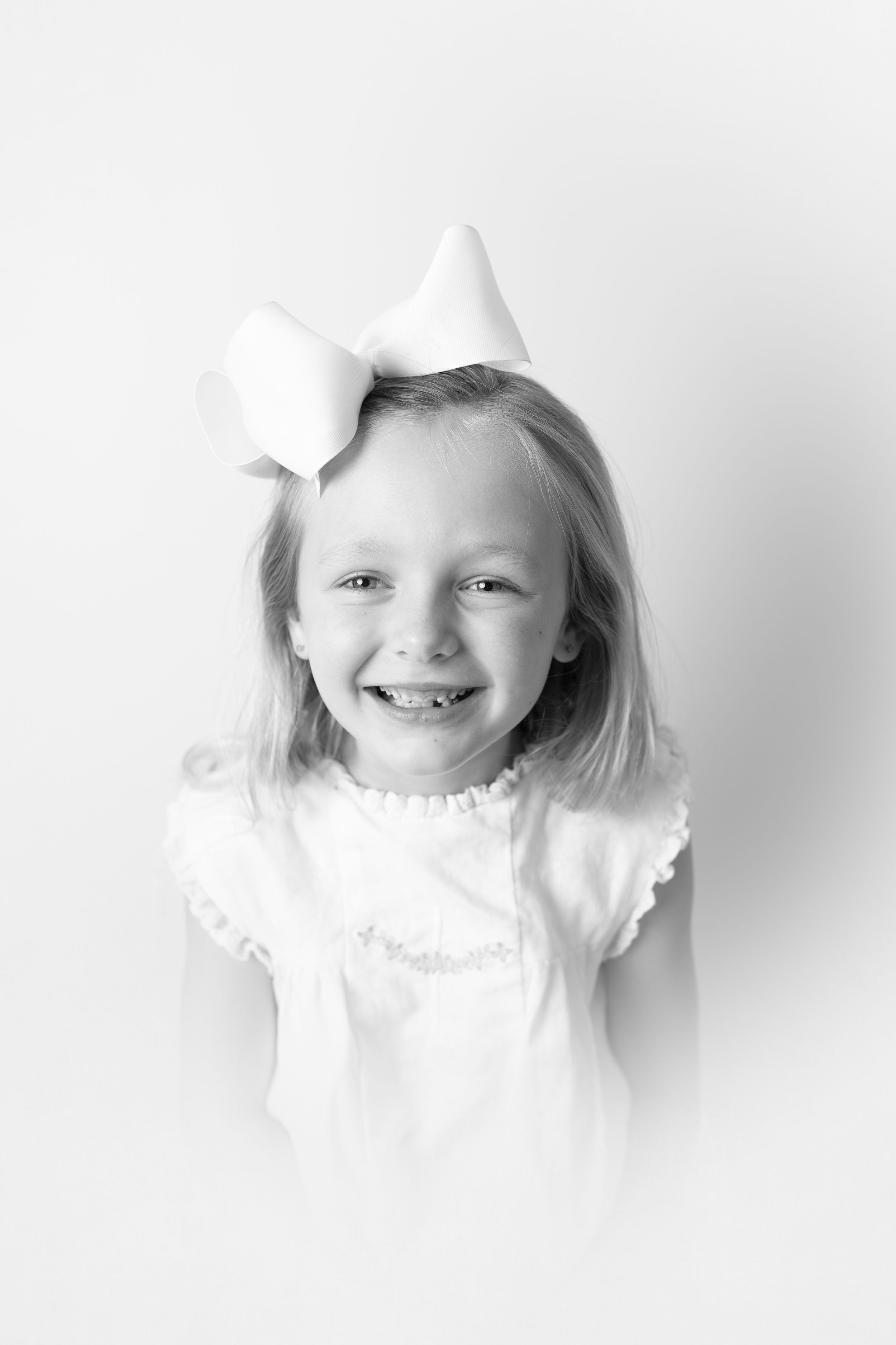 Close-up portrait of child in white ruffled dress against white background.