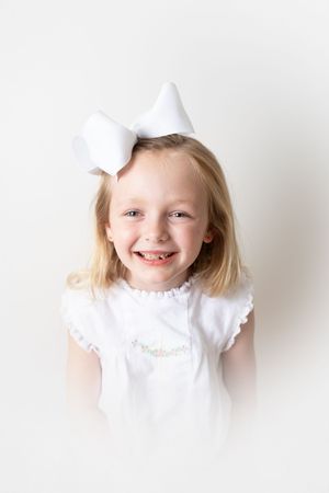 Child in white ruffled dress smiling against white background.