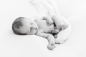 Artistic black and white photograph of sleeping newborn on white background.