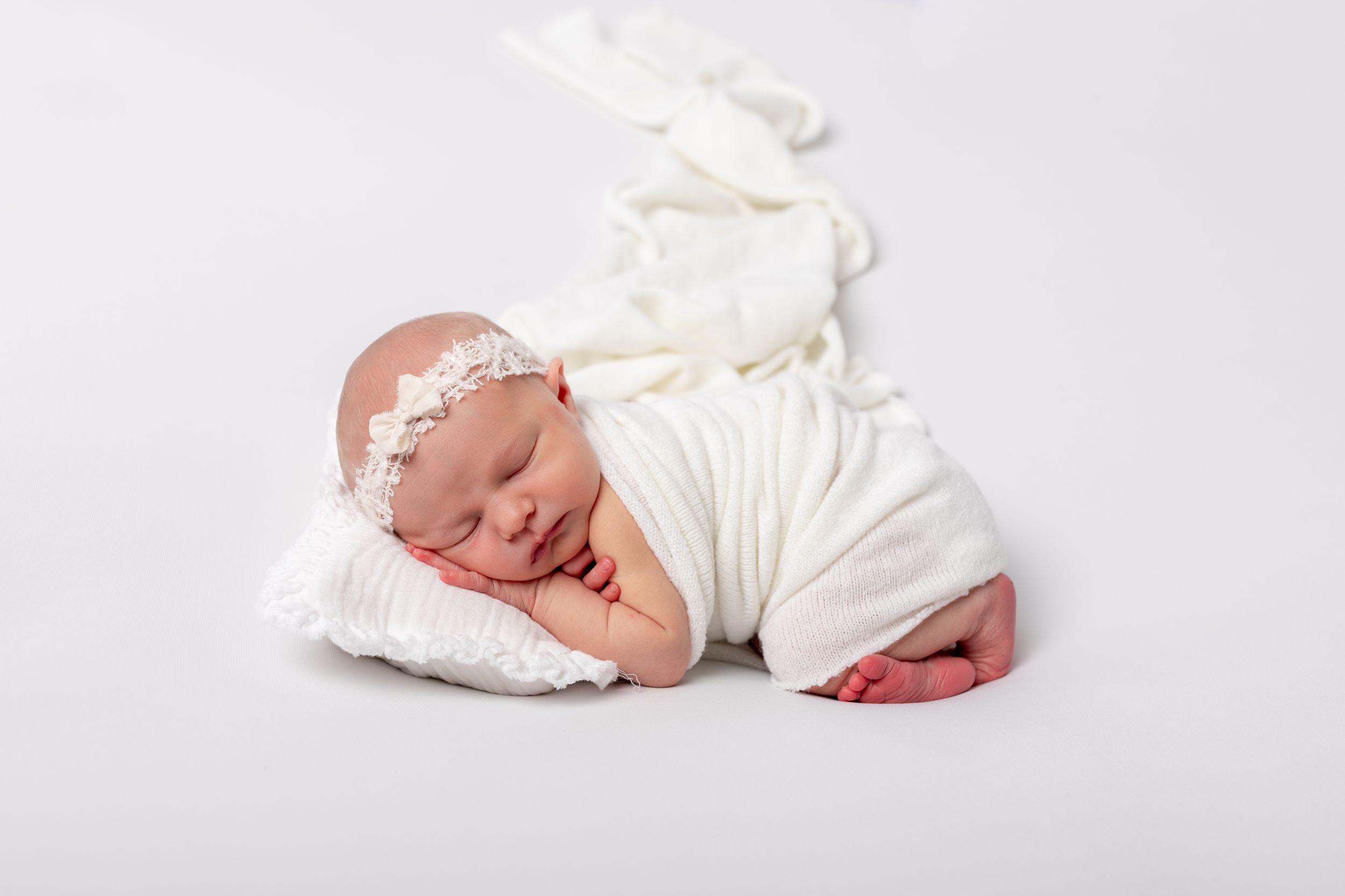 Newborn baby in white wrap sleeping on light colored background.