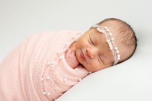 Sleeping newborn wrapped in pink swaddle blanket on white background.