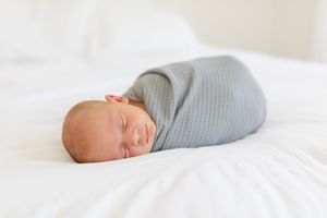 Peaceful newborn baby sleeping on soft white bedding in natural light.
