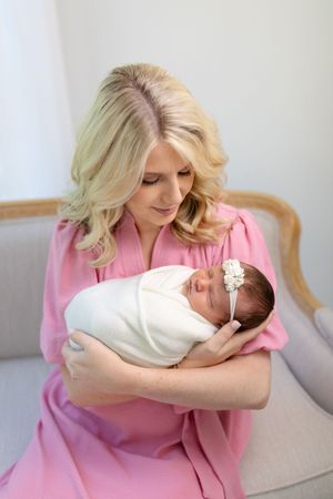 Woman in pink robe holding newborn baby in white wrap.