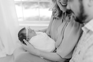 Couple smiling while holding newborn baby in natural light setting.