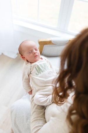 Baby in white outfit lying on bed in sunlit room.