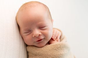 Sleeping newborn wrapped in beige blanket on white background.