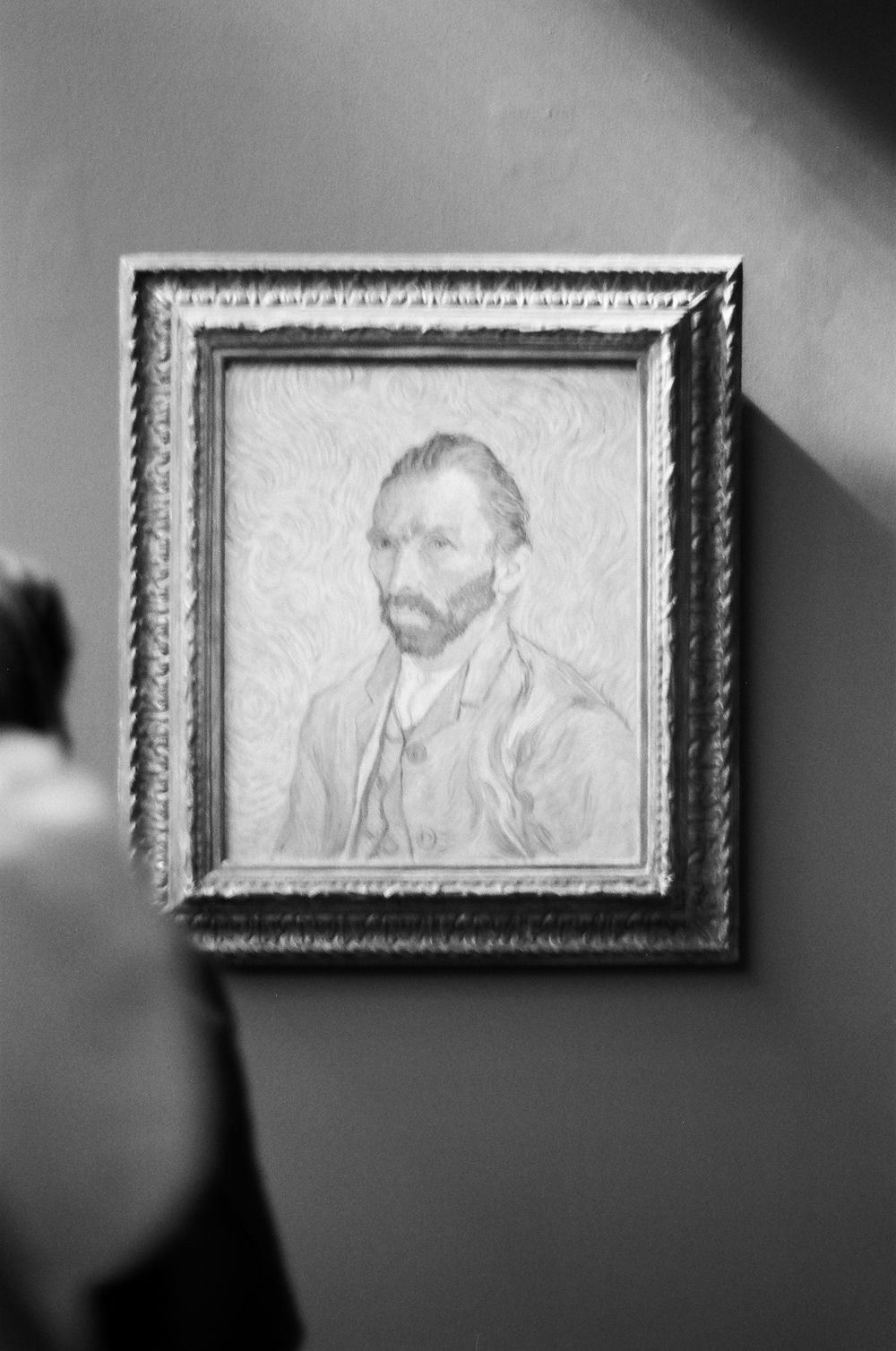 A framed black and white self-portrait drawing in an ornate frame hangs on a wall with dramatic lighting.