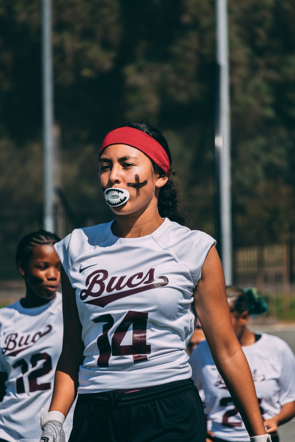 An athlete in a Bucs jersey number 14 with face paint and red headband stands on the field.