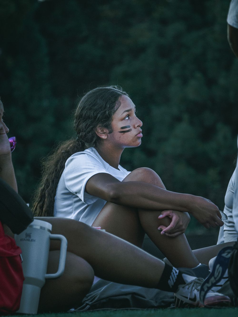 Athletes stretch and prepare for practice on the sidelines of a sports field.