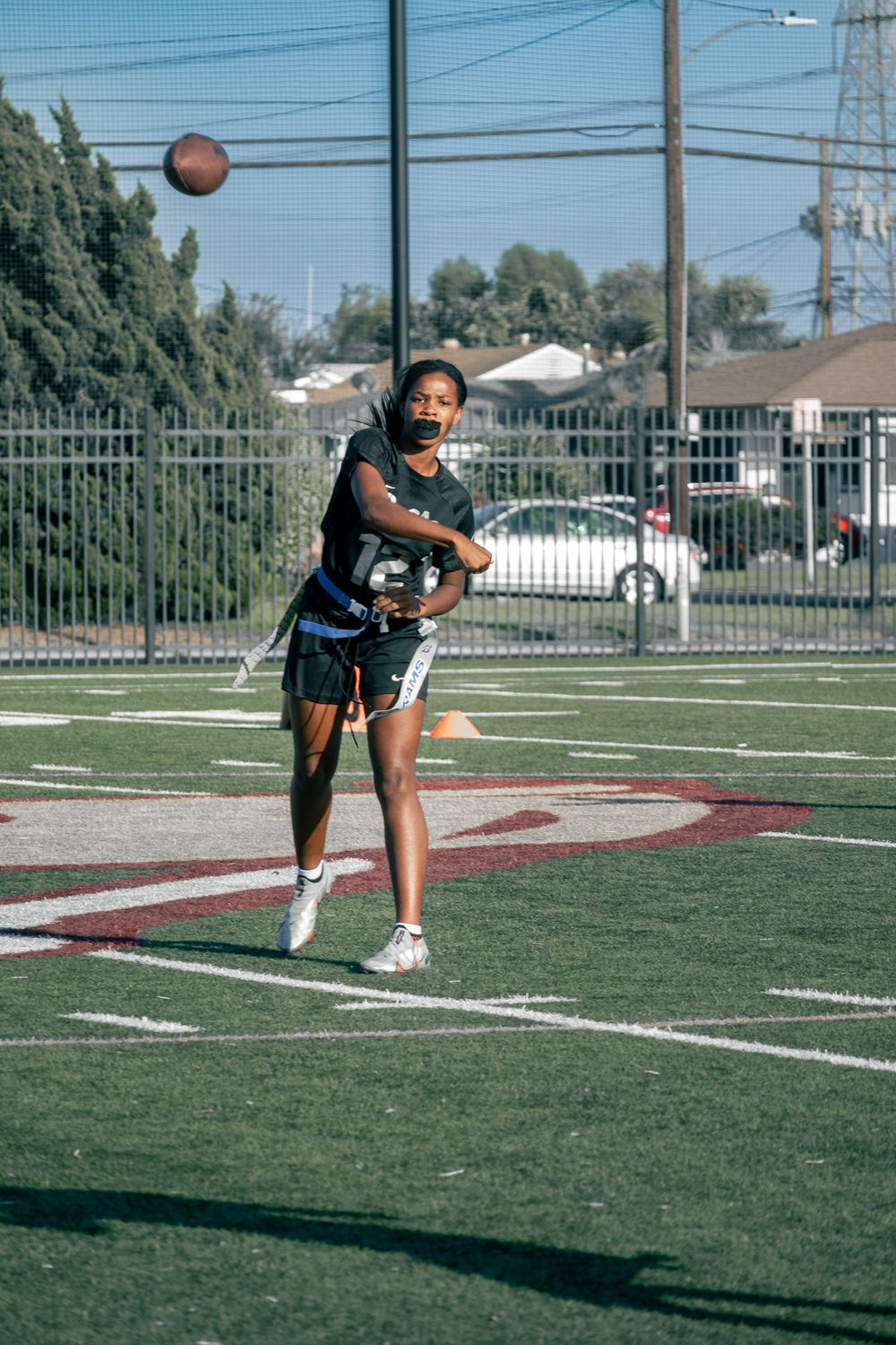 An athlete practices throwing a football on a sports field with power lines and buildings in the background.