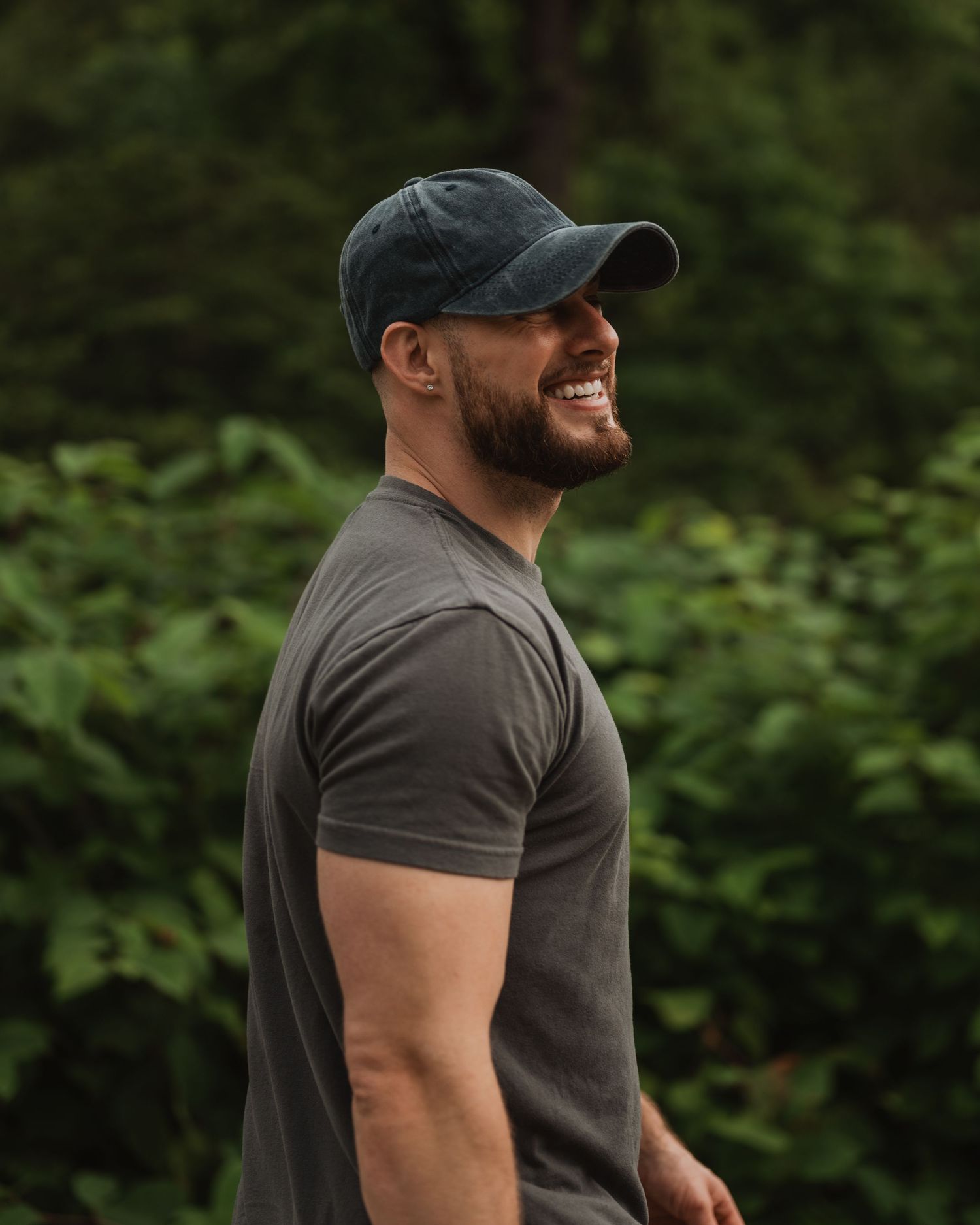 Athletic person in charcoal shirt and baseball cap smiling while working out in outdoor natural setting.