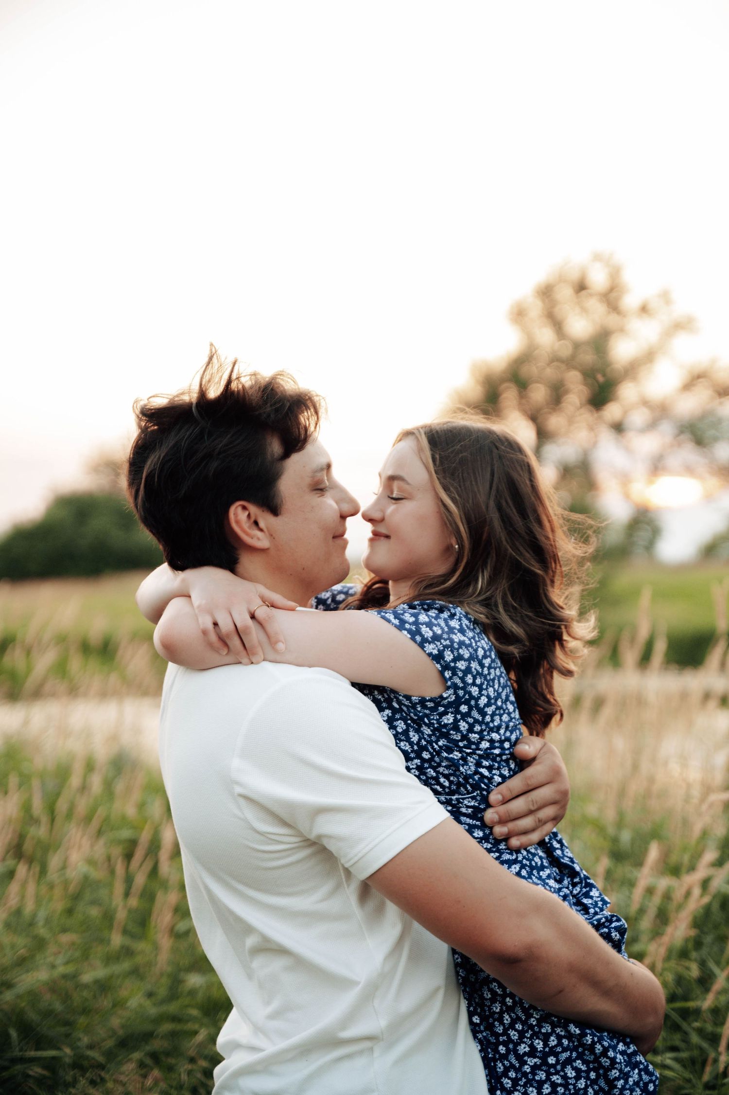 Romantic couple embraces in tall grass field during golden sunset hour.