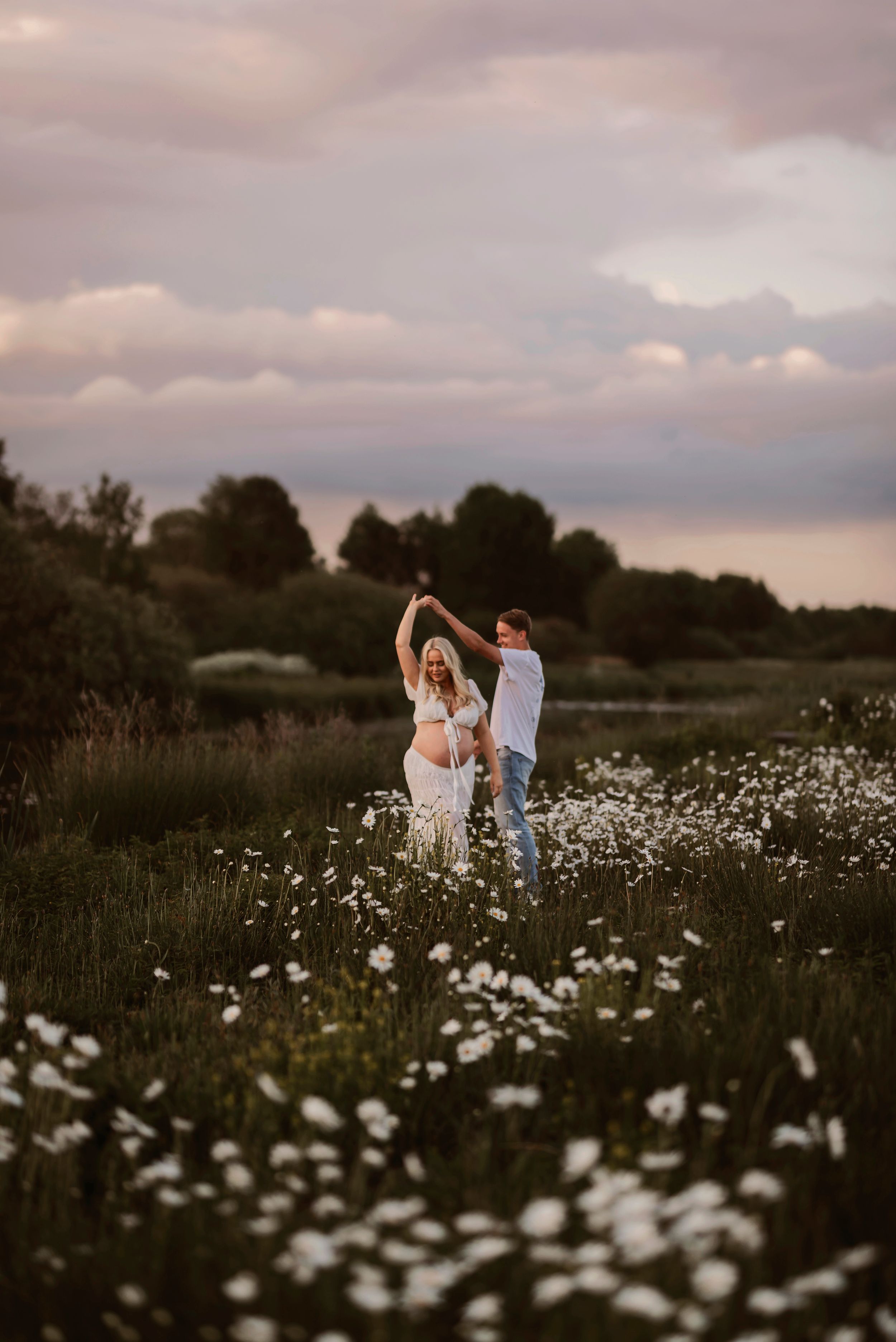 Romantiskt par dansar i blomsteräng vid solnedgången i Skåne nära Hässleholm – med dramatiska moln som bakgrund.