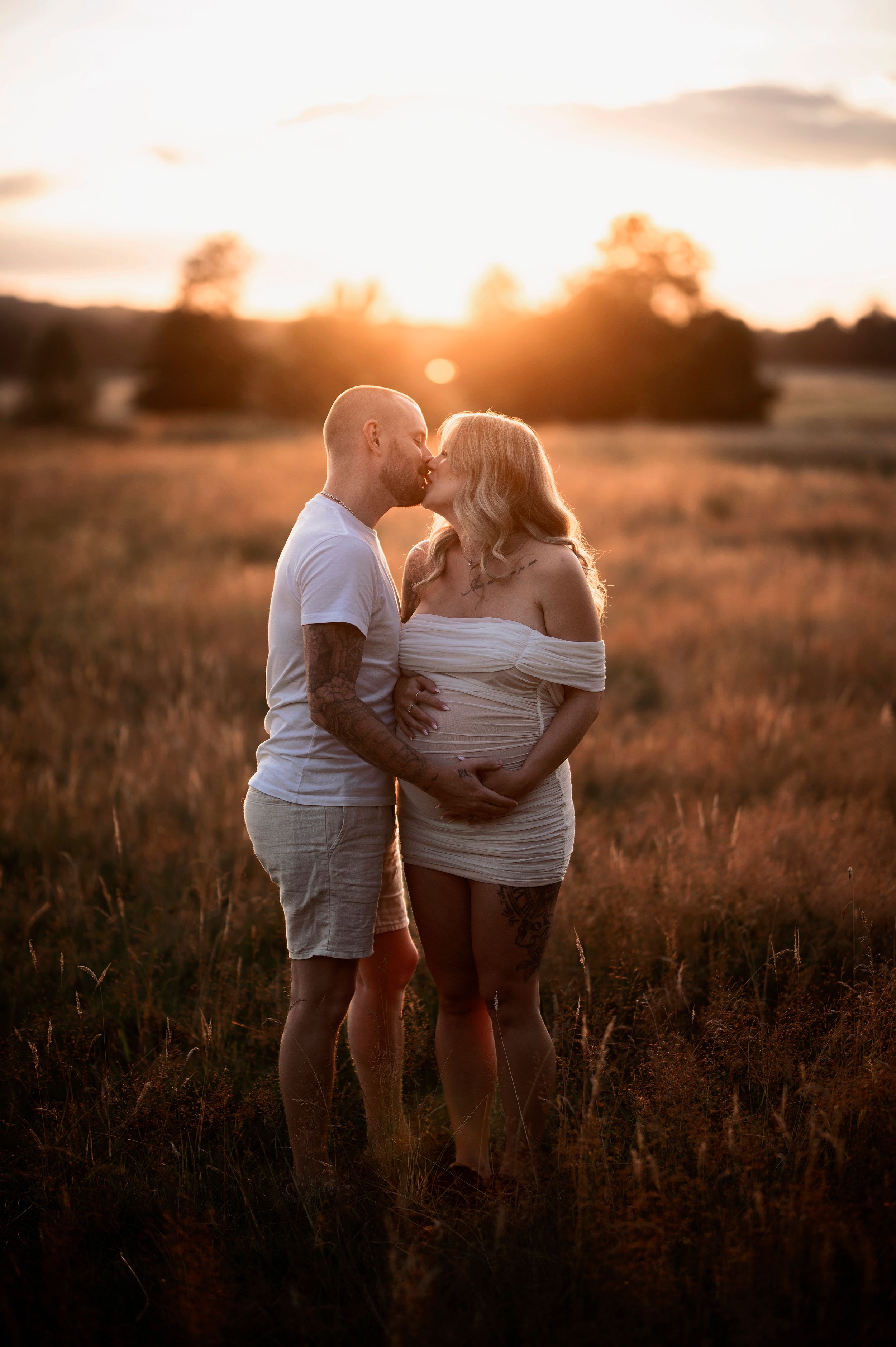 Gravid par i Skåne delar en intim stund i ett solbelyst fält nära Hässleholm – fångat i golden hour under en romantisk fotografering.