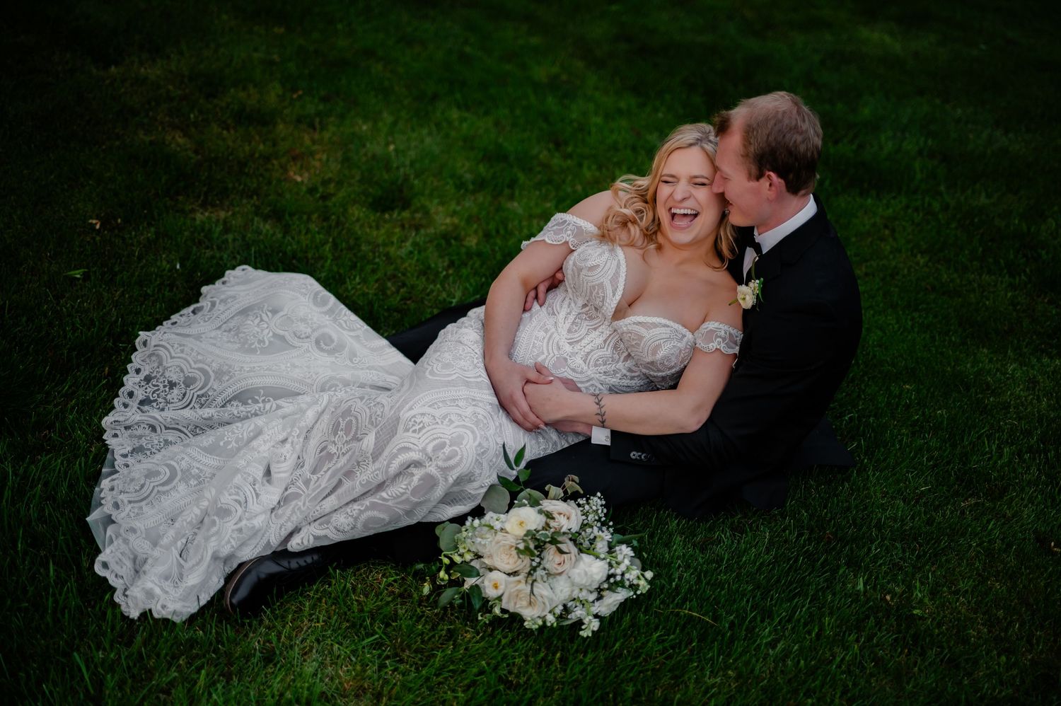 Romantic couple lying on lush green grass while embracing each other at their outdoor Grand Rapids wedding