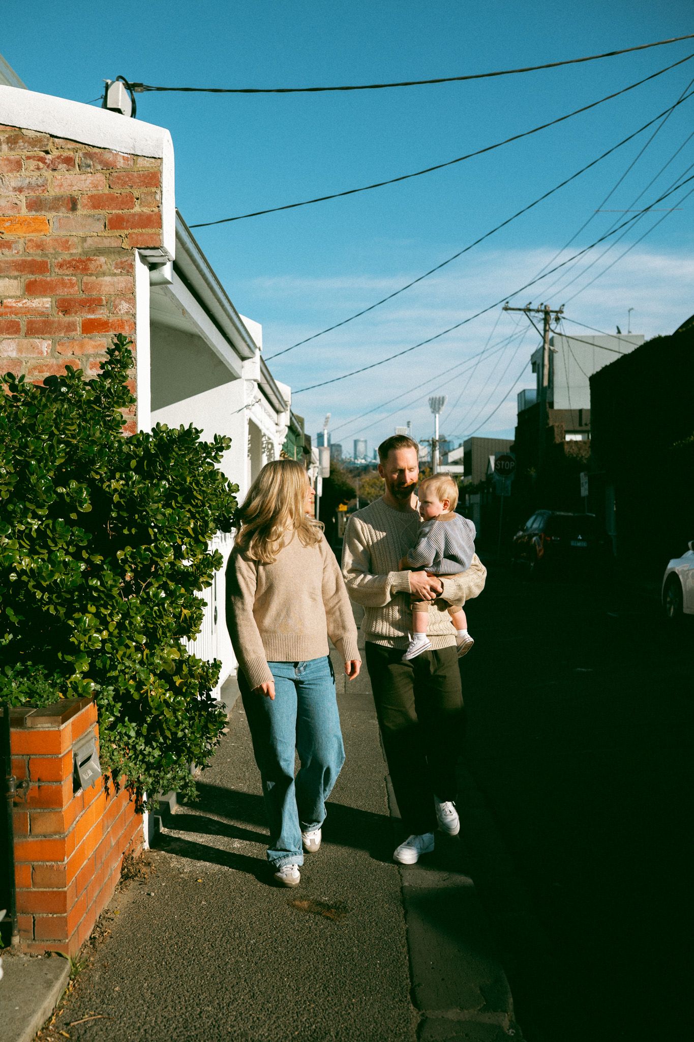 People stand against a red brick building wall casting shadows on a sunny day with vibrant blue sky.
