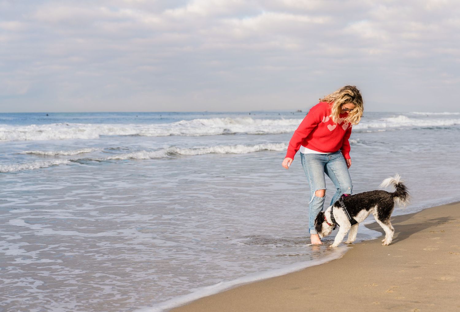 A woman and a dog enjoy a sunny day walking along shoreline of Huntington Beach in Orange County, California.