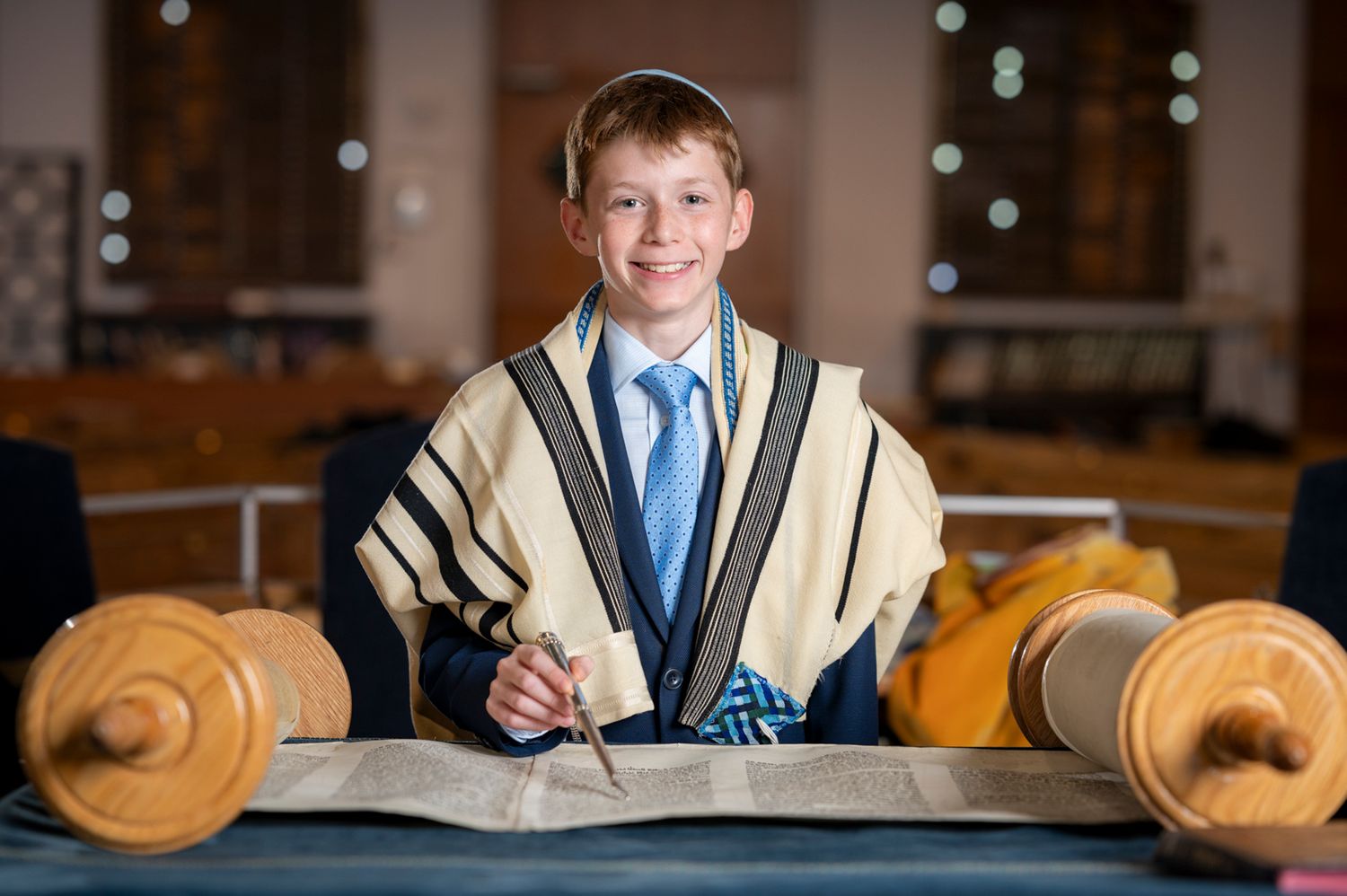 Classic portrait of a Bar Mitzvah boy wrapped in a tallit, standing in front of a Torah scroll at Shaarei Tefillah Synagogue.