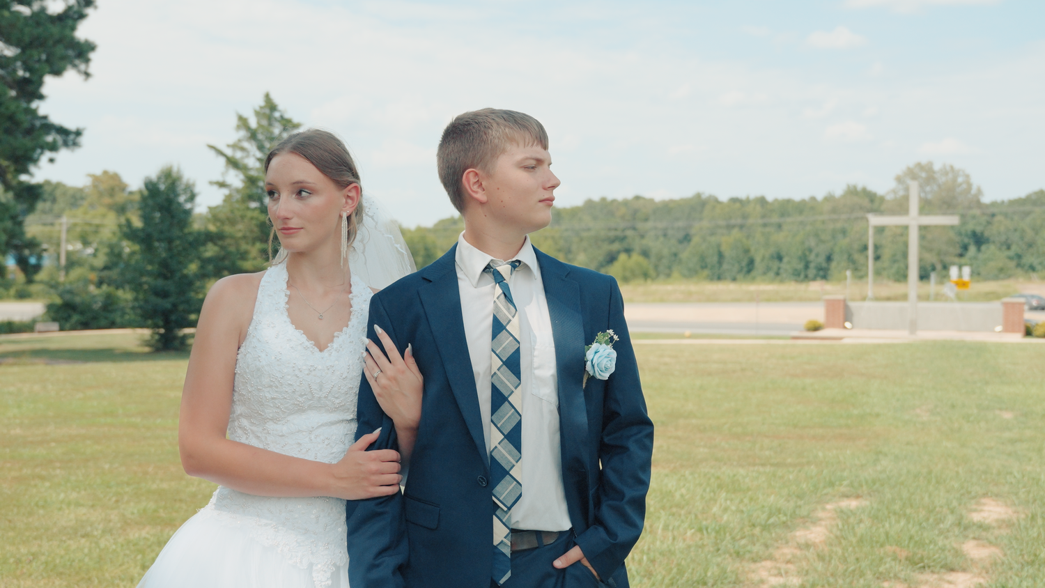 A wedding couple poses together on a grassy field during their outdoor wedding photoshoot session.