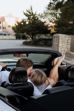 A romantic moment captured in a convertible car at sunset with stone architecture in the background.