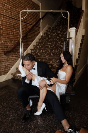 A set of five dramatic black and white photos show a couple in formal attire seated on steps against a brick wall.