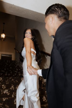 Couple in formal attire share a romantic moment in a hallway with decorative wallpaper and lighting.