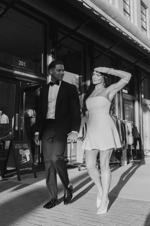 A stylish couple in black and white attire walking down a city sidewalk past storefronts.