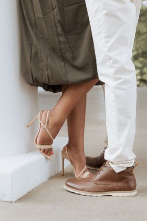 Low angle shot of feet showing contrasting brown leather shoes and white strappy heels during an outdoor event.