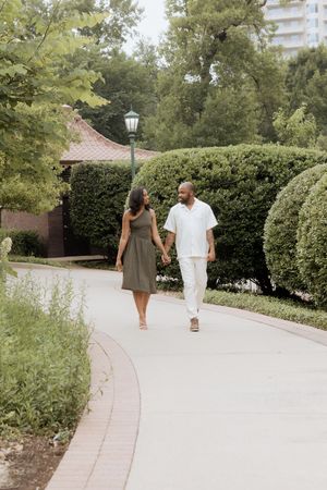 Two people walking hand in hand down a winding garden path surrounded by lush greenery and a vintage lamppost.