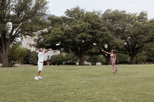 Multiple golfers playing on a spacious grassy park area surrounded by mature trees.