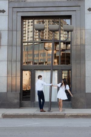 Two people in business attire interact near a modern office building entrance with glass doors and stone walls.