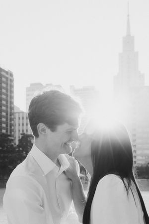 A romantic couple embraces and laughs together in black and white against a sunlit urban backdrop.